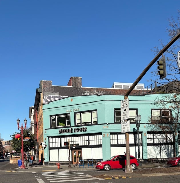 A two-story building on a corner, painted turquoise. It says Street Roots above the door.