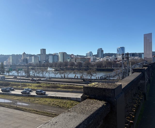 A view of the skyline of the west side, seen across the river. In the foreground, cars on a highway. The buildings are mostly of moderate height with one very tall pink building on the righthand side of the frame.