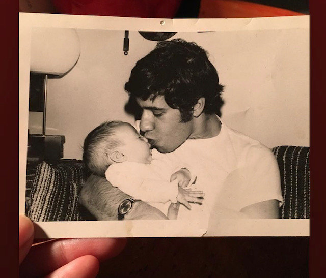 A young Jewish man with wavy black hair cradles an infant and kisses her on the nose. Black and white photo