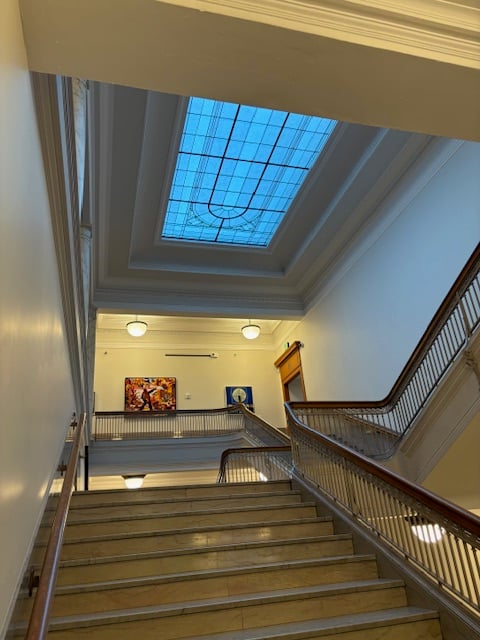 A rectangular skylight with an oval ornamental design seen from the bottom of the final set of stairs befoe the top floor.